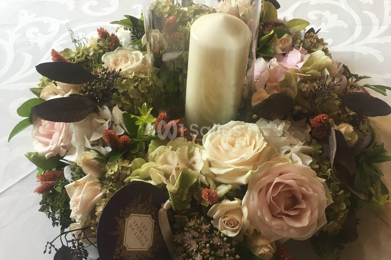 Centre de table floral avec roses, hortensias et feuillages, entourant une bougie blanche cylindrique.