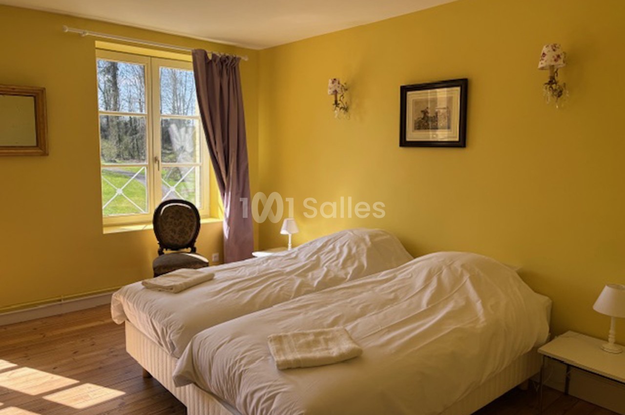 Deux lits simples avec draps blancs dans une chambre lumineuse aux murs jaunes, vue sur un jardin par une fenêtre.