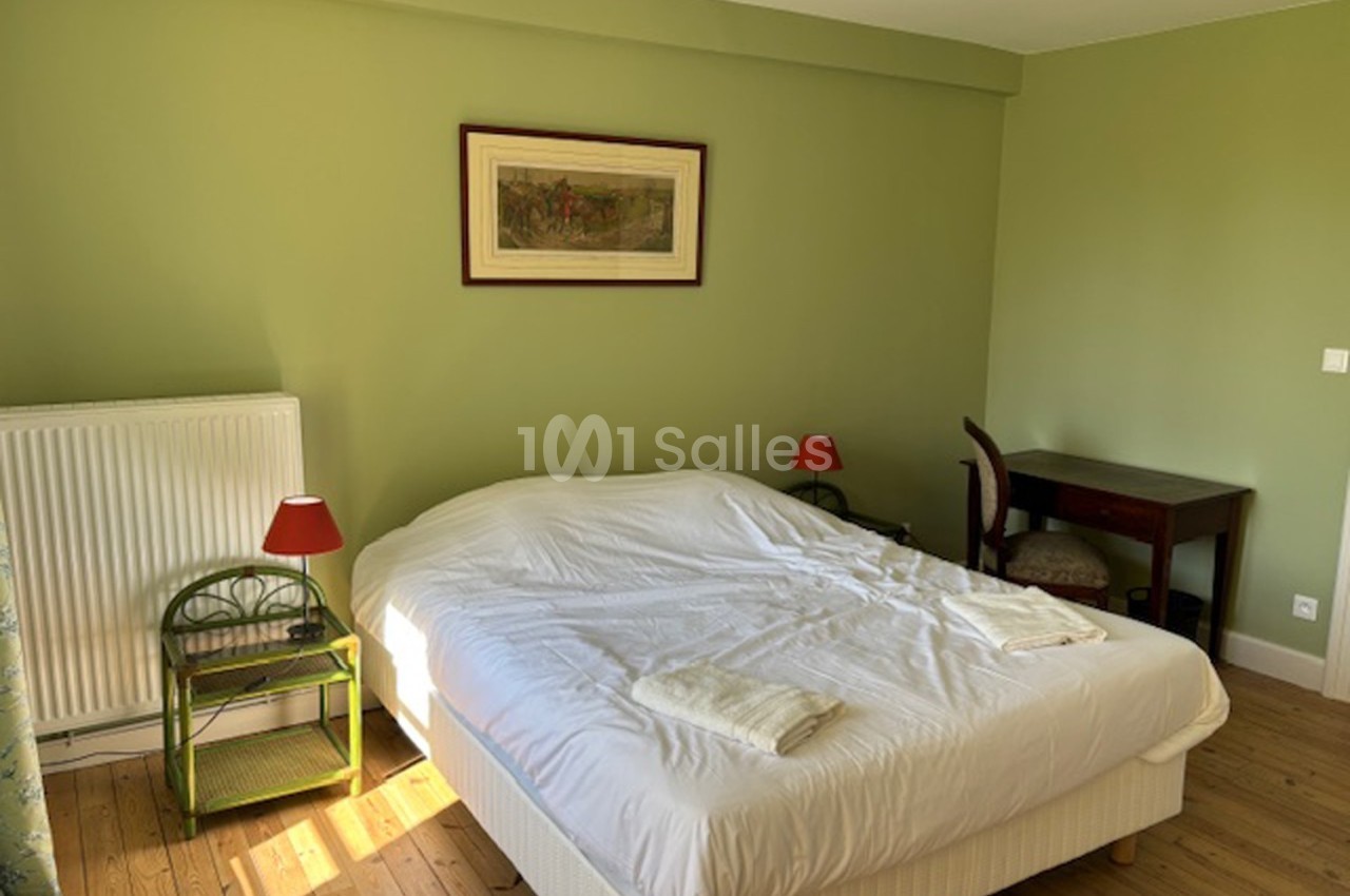 Chambre avec lit double, murs verts, bureau en bois, deux lampes rouges et parquet en bois clair.