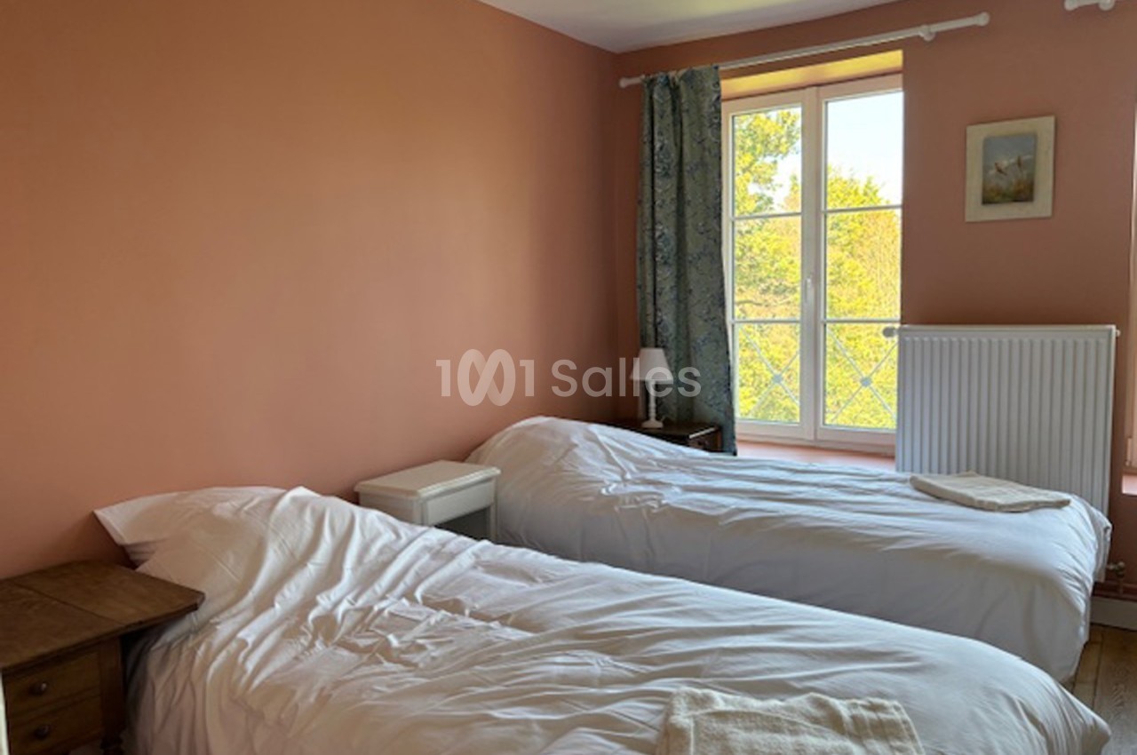 Deux lits simples avec draps blancs dans une chambre aux murs pêche, éclairée par une fenêtre donnant sur un paysage…
