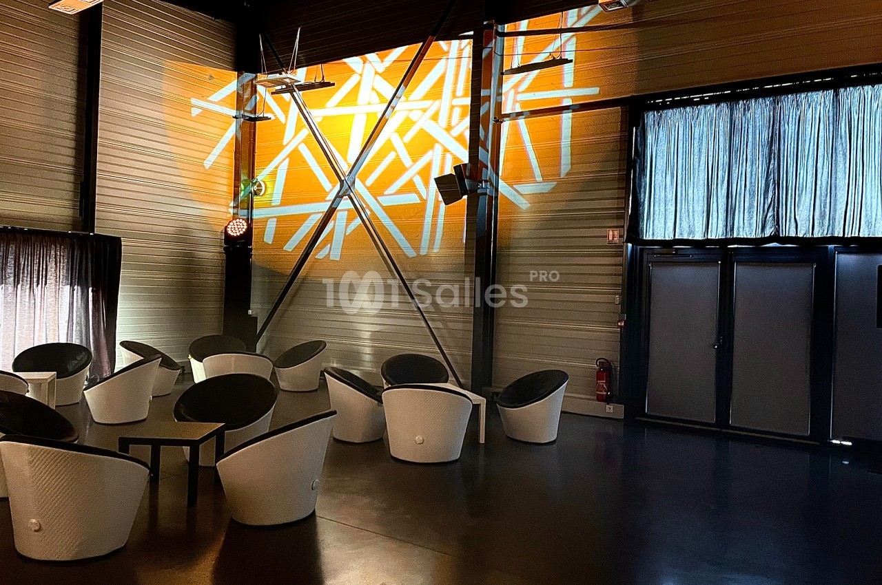 Salle moderne avec des fauteuils blancs, éclairage mural géométrique orange et rideaux couvrant des fenêtres.