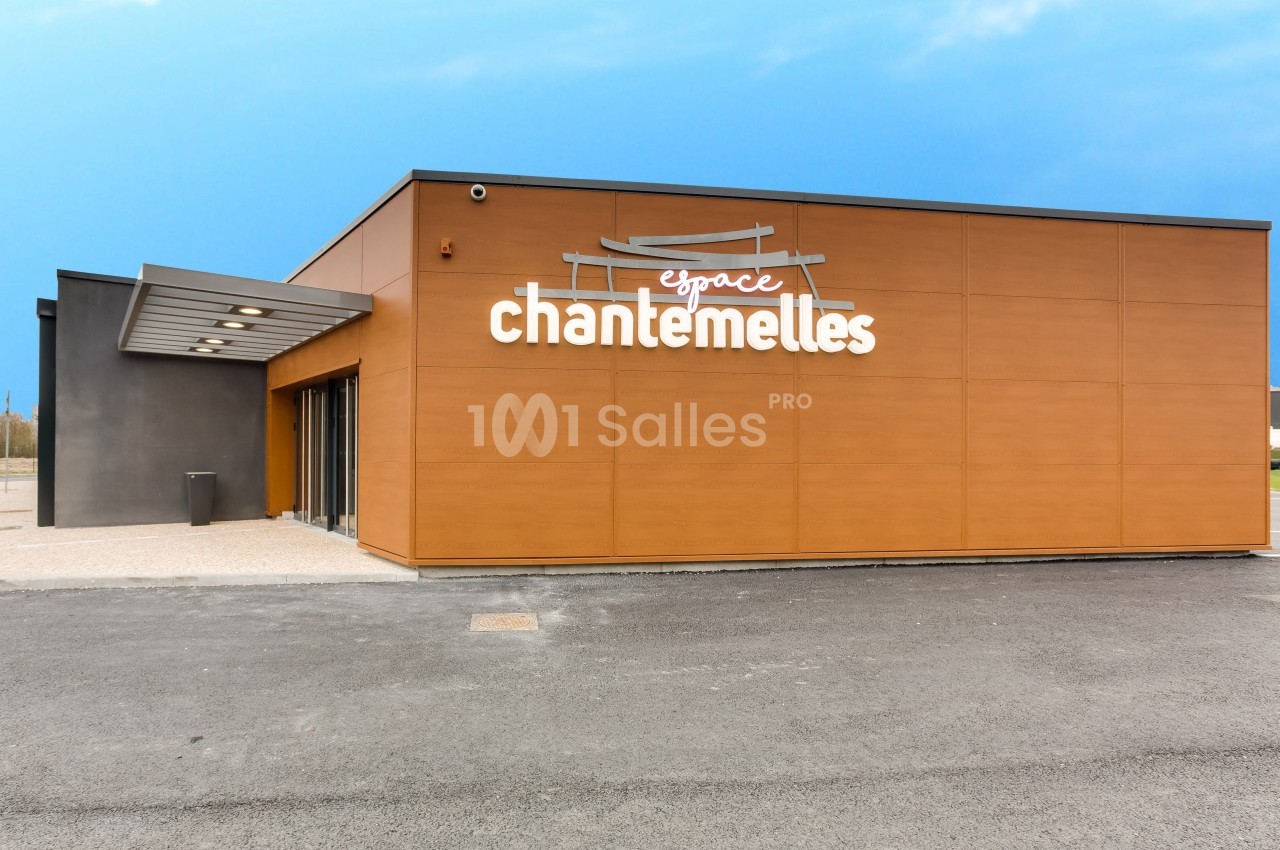 Façade d'un bâtiment moderne avec revêtement en bois et enseigne ’Espace Chantemelles’ sur un parking asphalté.
