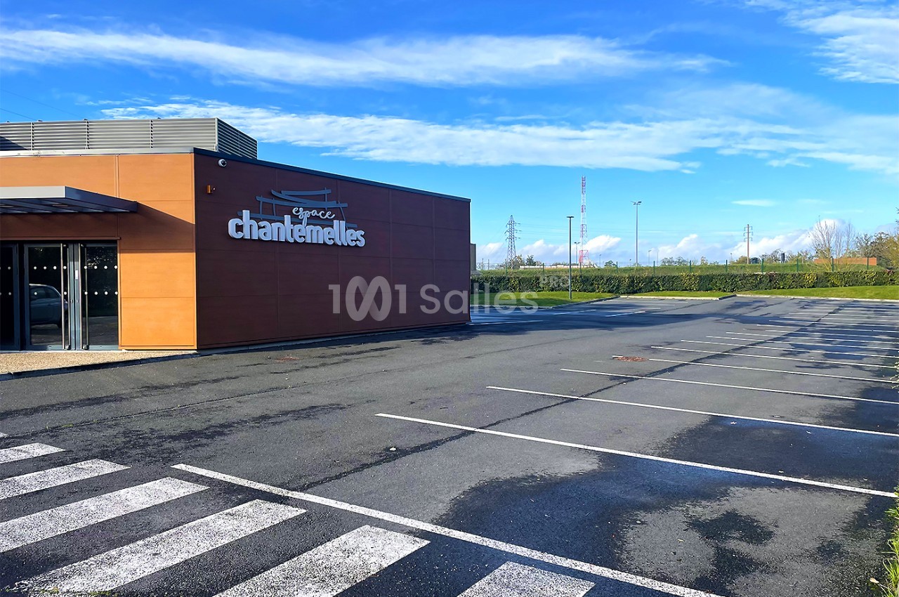 Façade d'un bâtiment moderne avec parking vide et passage piéton, ciel dégagé en arrière-plan.