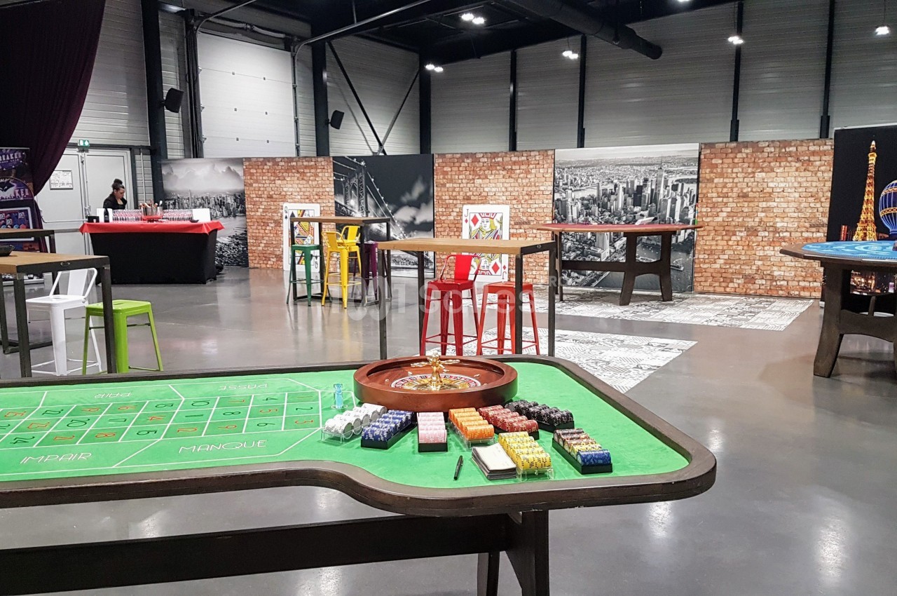 Salle aménagée avec des tables de jeux de casino, des chaises colorées et un décor mural urbain.