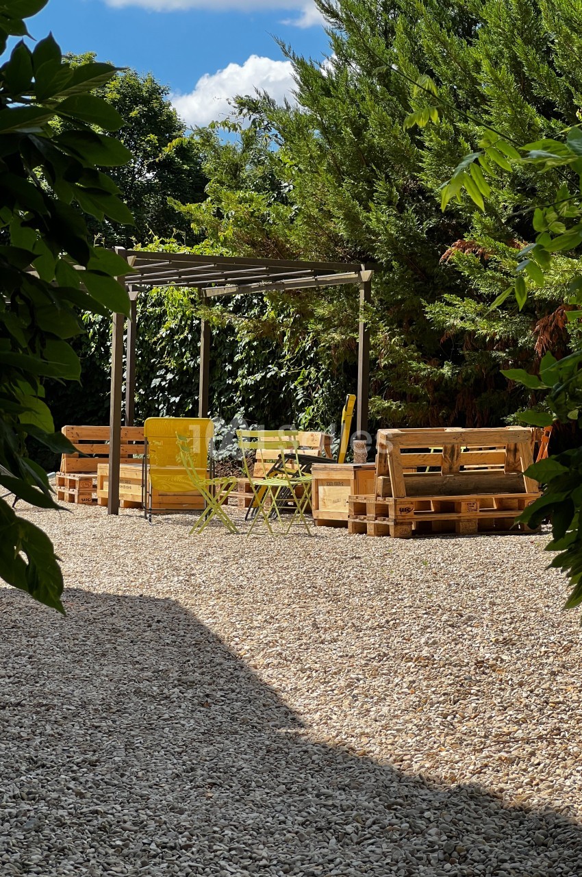 Espace extérieur avec salon de jardin en palettes, chaises jaunes et pergola, entouré de végétation.