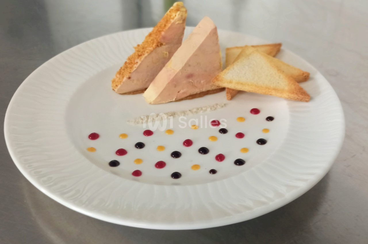 Assiette de foie gras en tranches avec toasts triangulaires et décor de sauces colorées sur une table en métal.