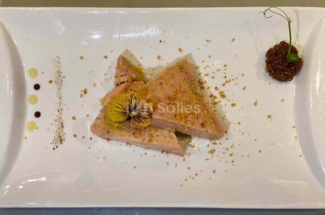 Tranches de foie gras décorées d'une fleur comestible, accompagnées de condiments sur une assiette blanche.