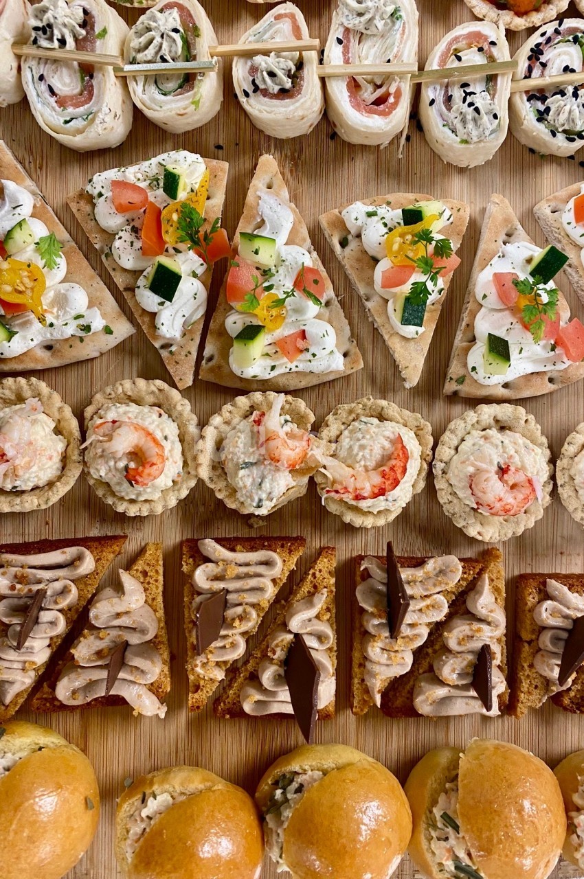 Plateau de canapés variés comprenant bouchées salées, tartines garnies et mini-brioches sur une planche en bois.