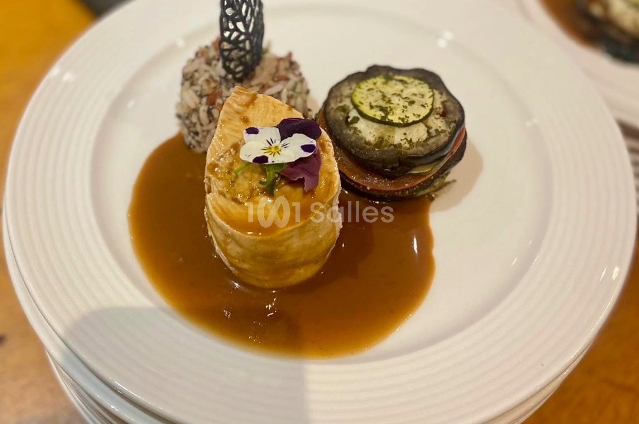 Assiette gastronomique avec feuilleté garni, légumes grillés, riz en boule et sauce, décorée d'une fleur comestible.