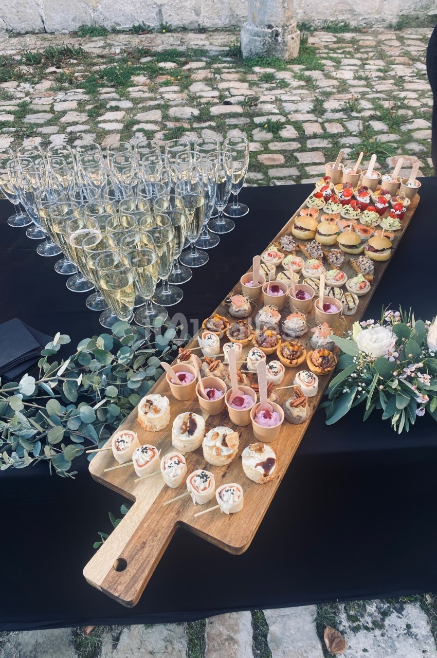 Plateau de bouchées apéritives variées avec flûtes de champagne alignées sur une table noire décorée de feuillage et fleurs.