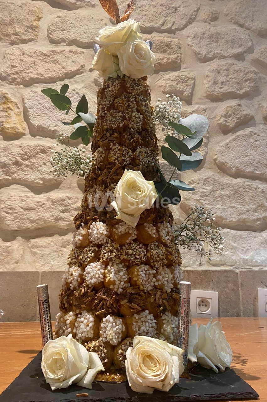 Pièce montée en choux caramélisés décorée de roses blanches et de feuillages, posée sur une table en bois.