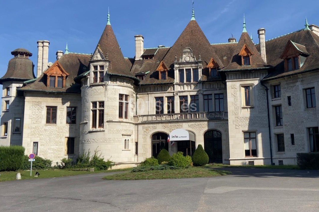 Façade d'un grand bâtiment historique en pierre avec plusieurs tours et toits en pente sous un ciel bleu.