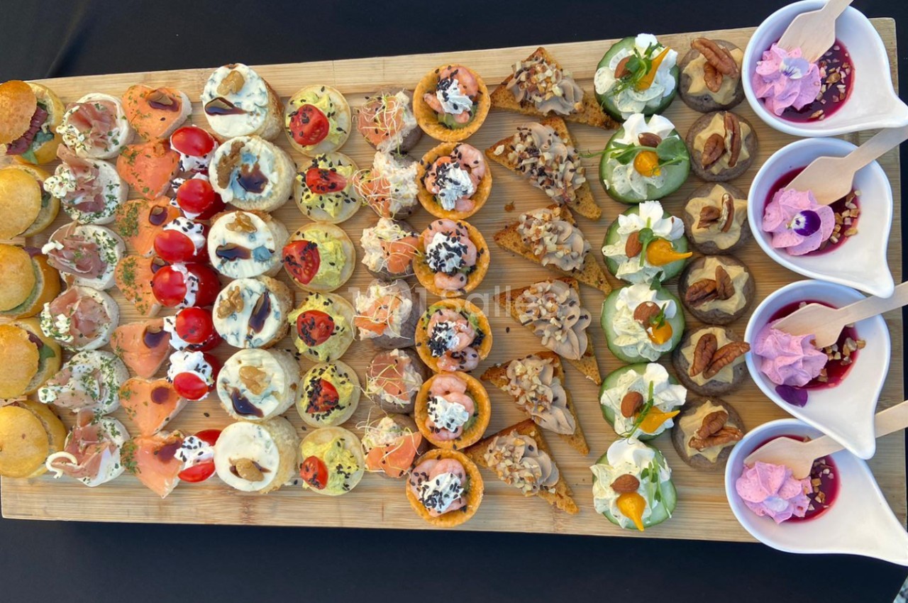 Plateau en bois garni d'un assortiment de bouchées salées et verrines sucrées, disposées en rangées colorées.