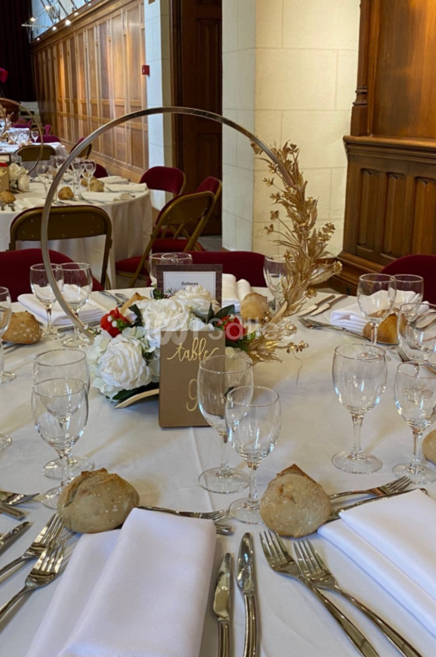 Table dressée pour un événement, avec nappes blanches, vaisselle élégante, centre de table floral et décor doré.