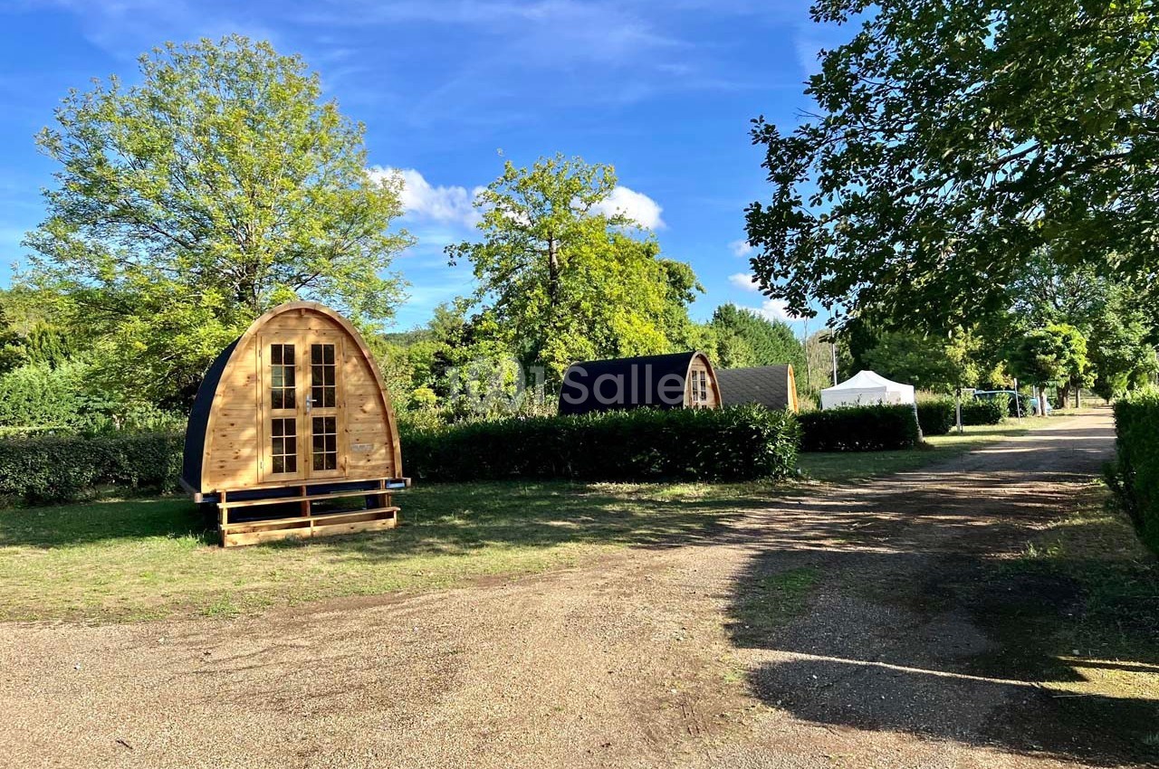 Deux cabanes en bois en forme d’arche dans un espace vert avec un chemin de gravier et des arbres environnants.