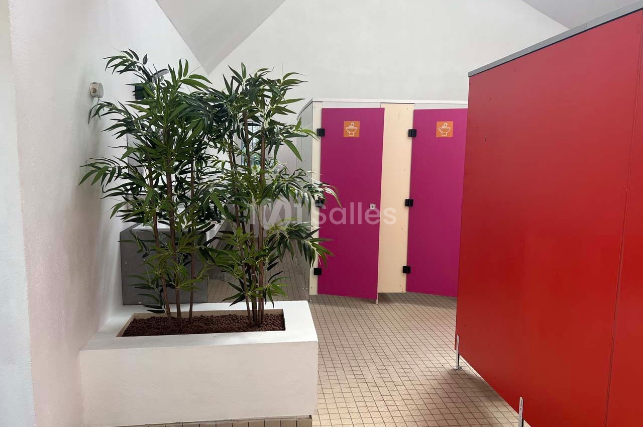 Plantes décoratives dans un espace intérieur avec des cabines de toilettes aux portes roses et rouges.