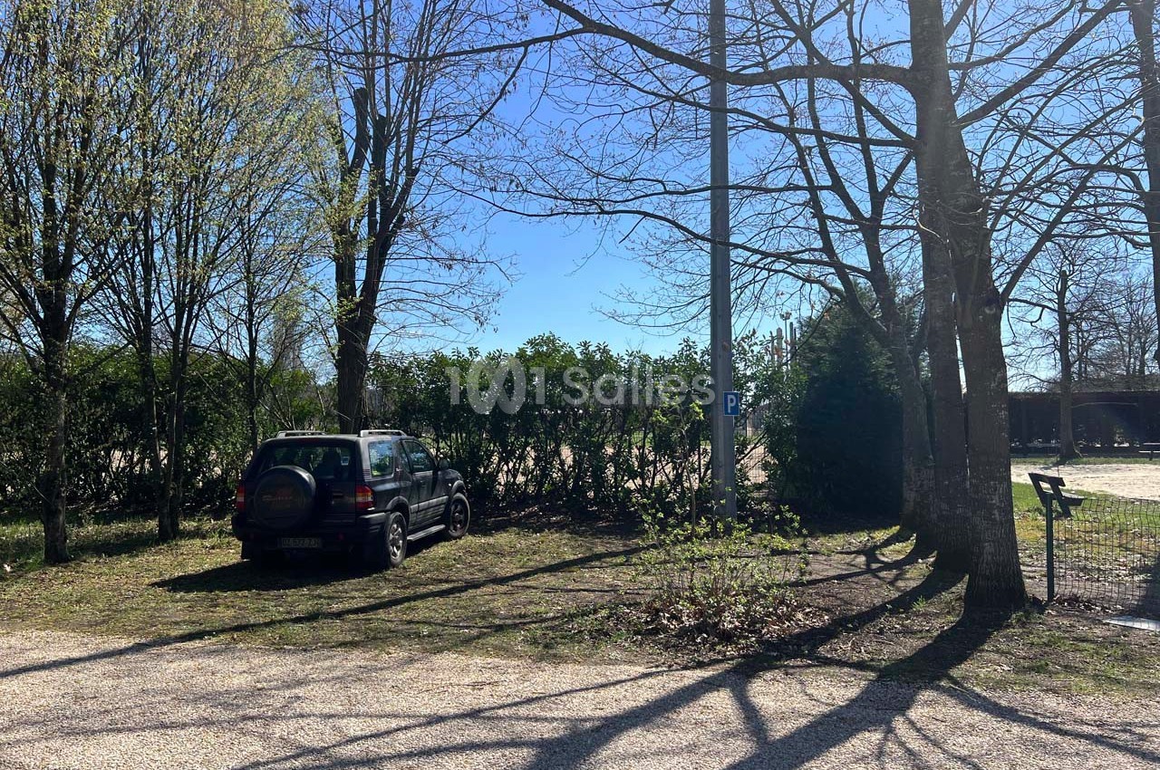 Voiture noire garée sur un espace herbeux près d'arbres, avec un ciel dégagé en arrière-plan.