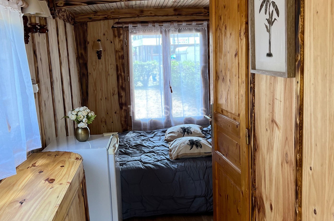 Chambre en bois avec un lit double, des rideaux blancs, une commode et un tableau décoratif sur le mur.
