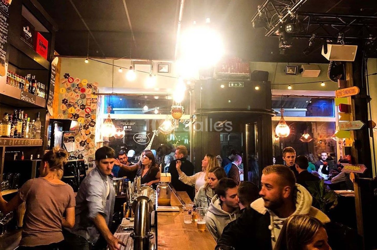 Des personnes discutent et consomment des boissons dans un bar animé avec un éclairage chaleureux.