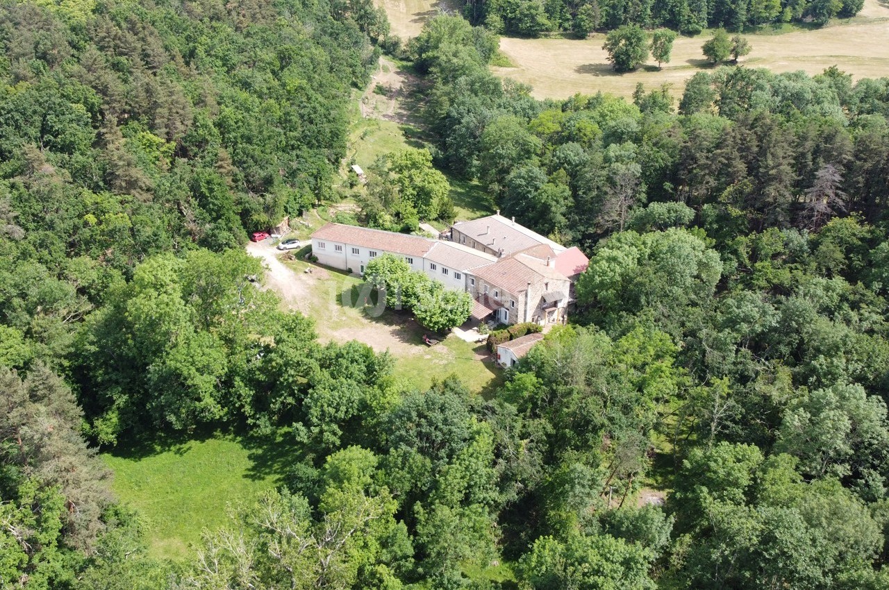 Vue aérienne d'un grand bâtiment entouré de forêt et de clairières verdoyantes.