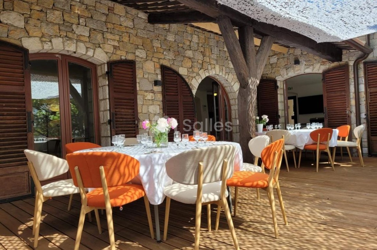 Terrasse en bois avec tables dressées, chaises colorées et ombrage partiel sous une pergola en pierre et bois.
