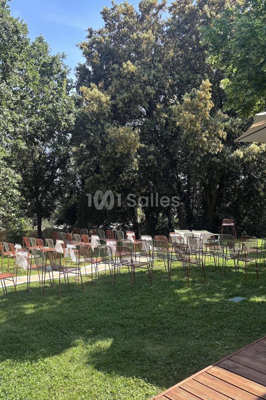 Chaises alignées sur une pelouse verte, disposées pour un événement en plein air, entourées d'arbres et de lumière naturelle.