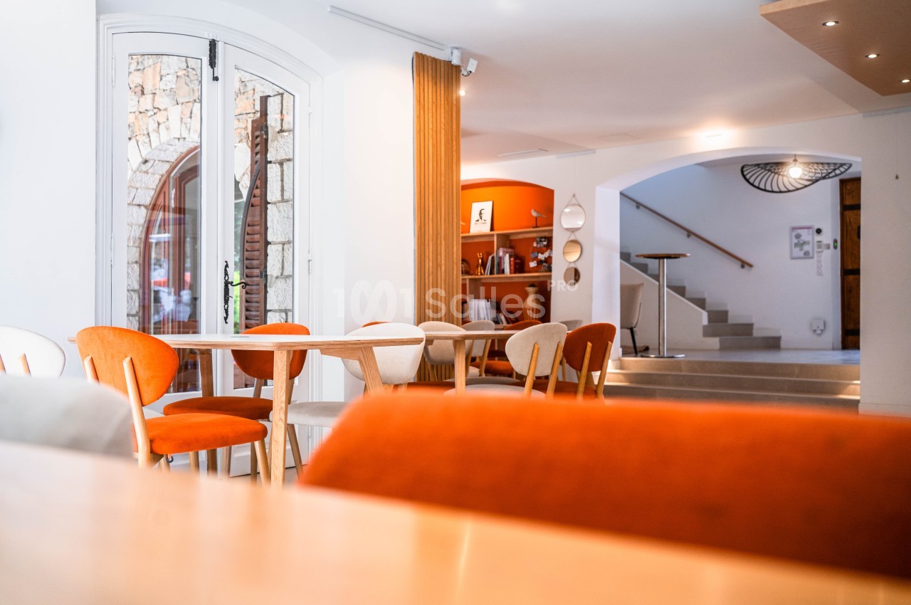 Intérieur contemporain avec chaises orange et table bois, escalier visible au fond.
