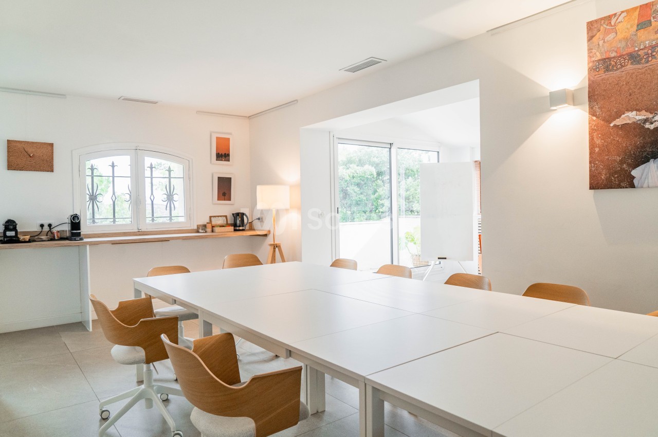 Salle lumineuse avec table blanche modulable, chaises caramel, accès terrasse et vue sur la verdure.
