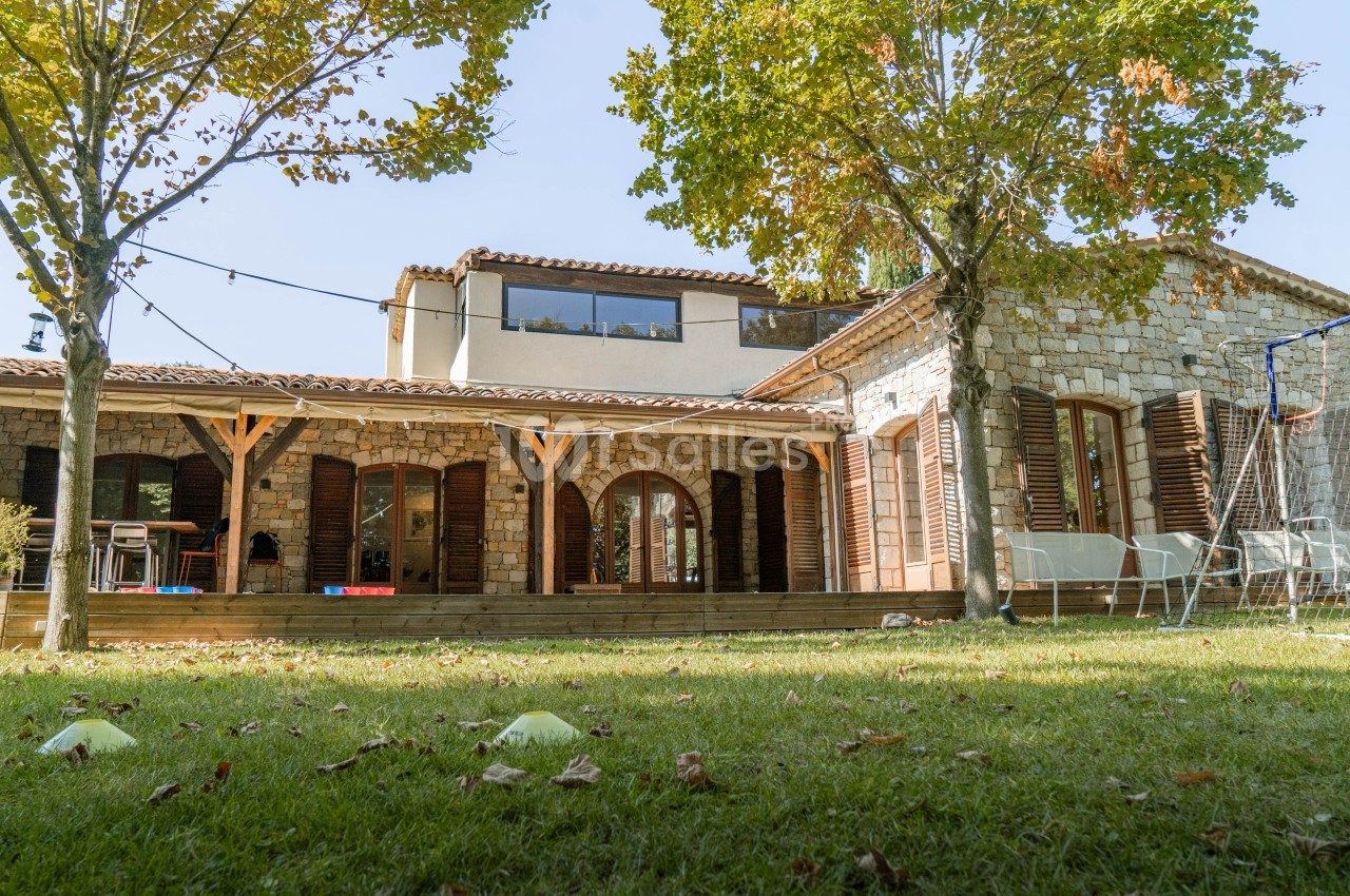 Maison en pierre avec terrasse couverte, portails en bois, jardin arboré et mobilier de détente.