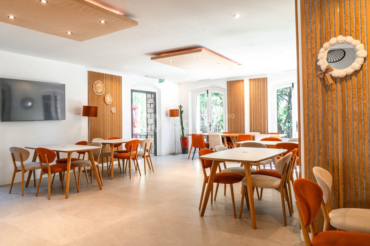 Salle lumineuse avec tables dressées, chaises orange et bois clair, baies vitrées, panneaux bois ajouré.