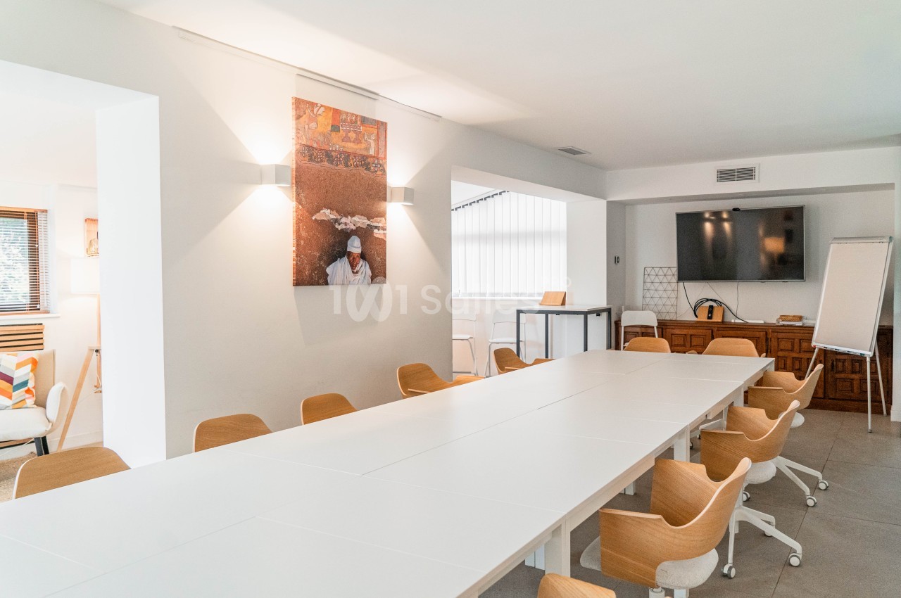Salle de réunion intérieure avec table blanche centrale, chaises en bois clair, écran mural et tableau blanc.