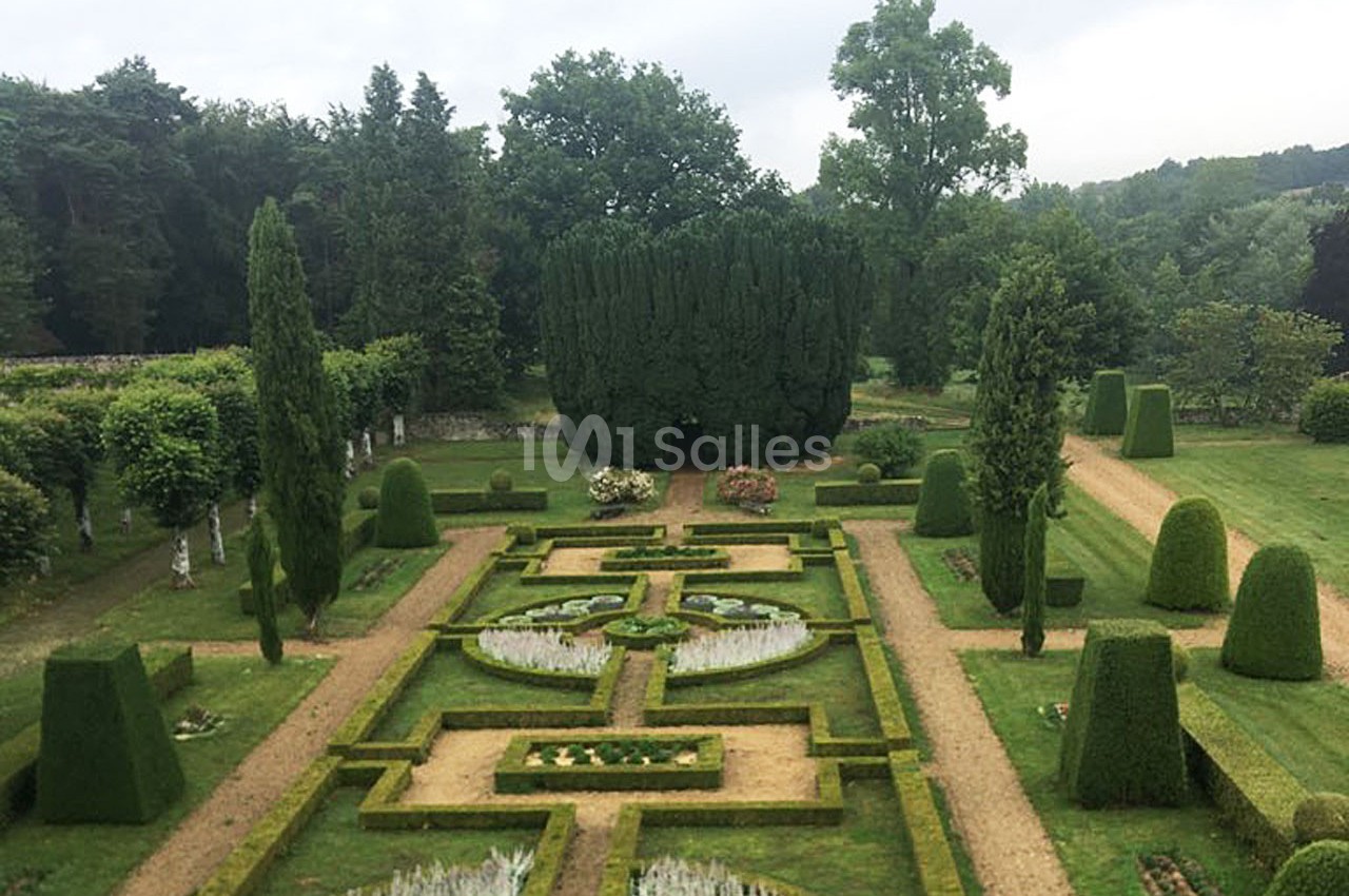 Jardin à la française avec parterres symétriques, allées de gravier et arbustes taillés, entouré de verdure.