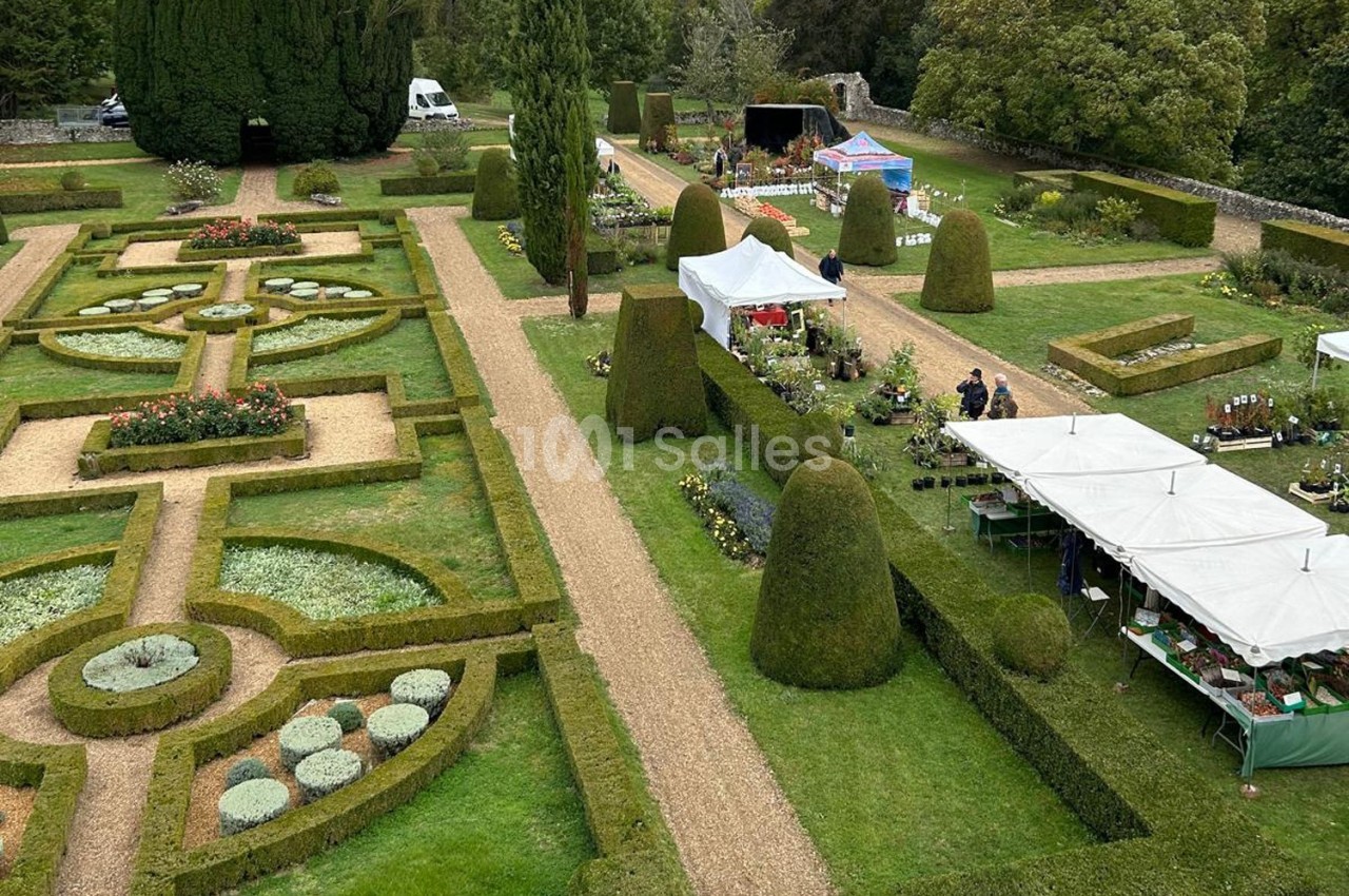 Jardin à la française avec allées gravillonnées, parterres géométriques et stands de marché en arrière-plan.