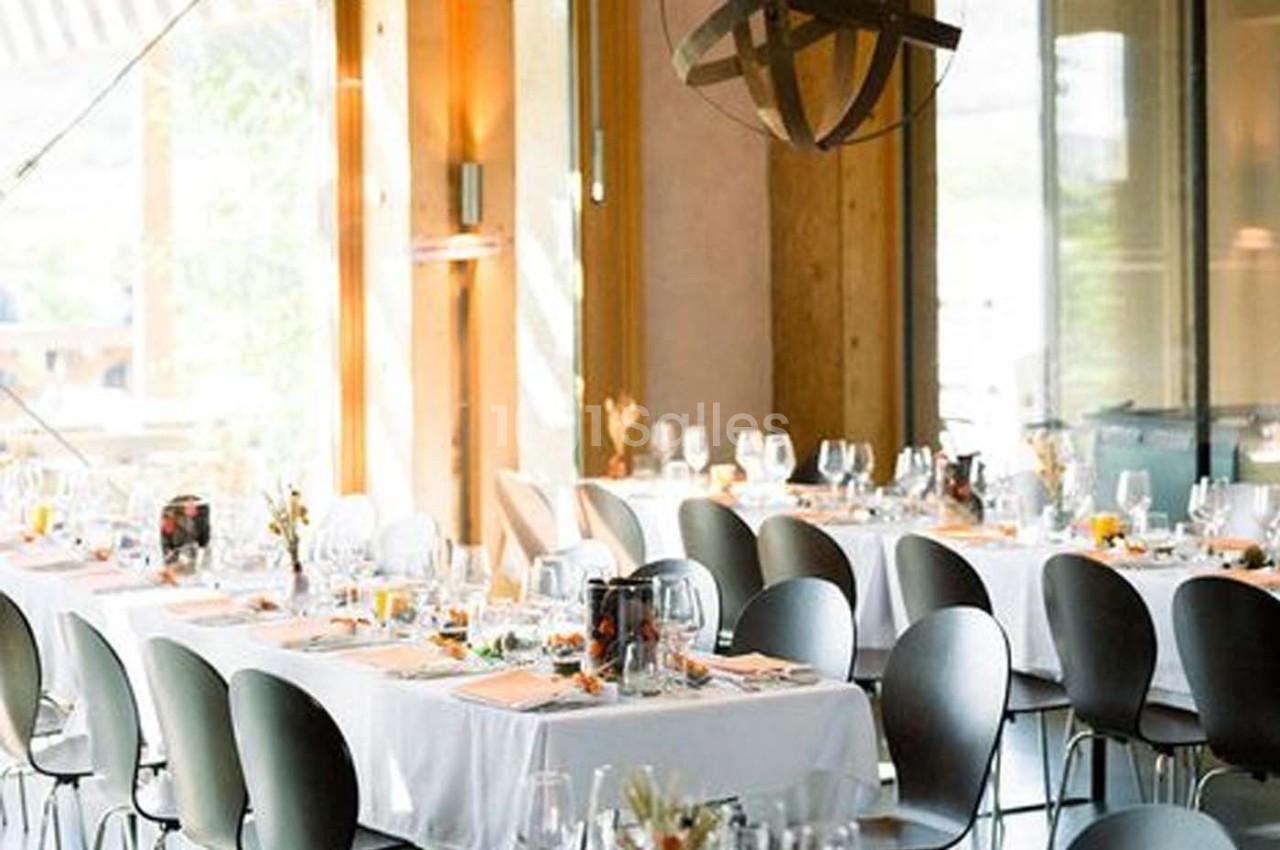Salle lumineuse avec tables dressées, nappes blanches, chaises modernes et décoration élégante pour un repas.