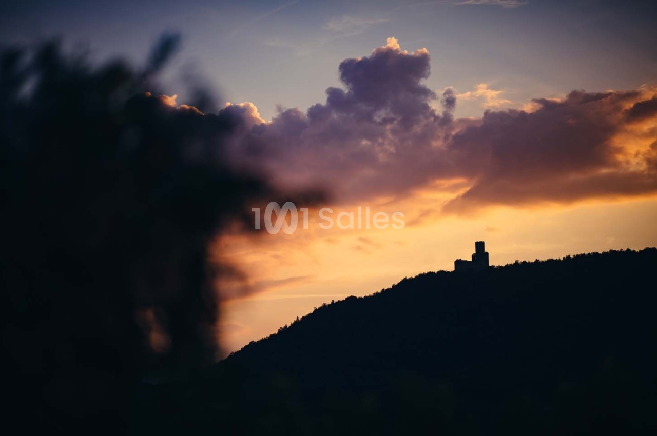 Silhouette d'une colline avec une tour au sommet, éclairée par un coucher de soleil aux teintes orange et violettes.