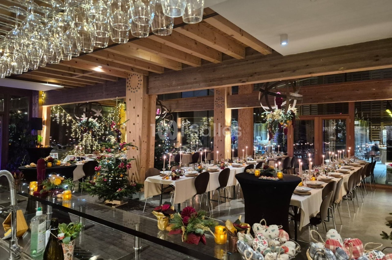 Salle de réception décorée pour un dîner festif, avec tables dressées, bougies allumées et sapin de Noël illuminé.
