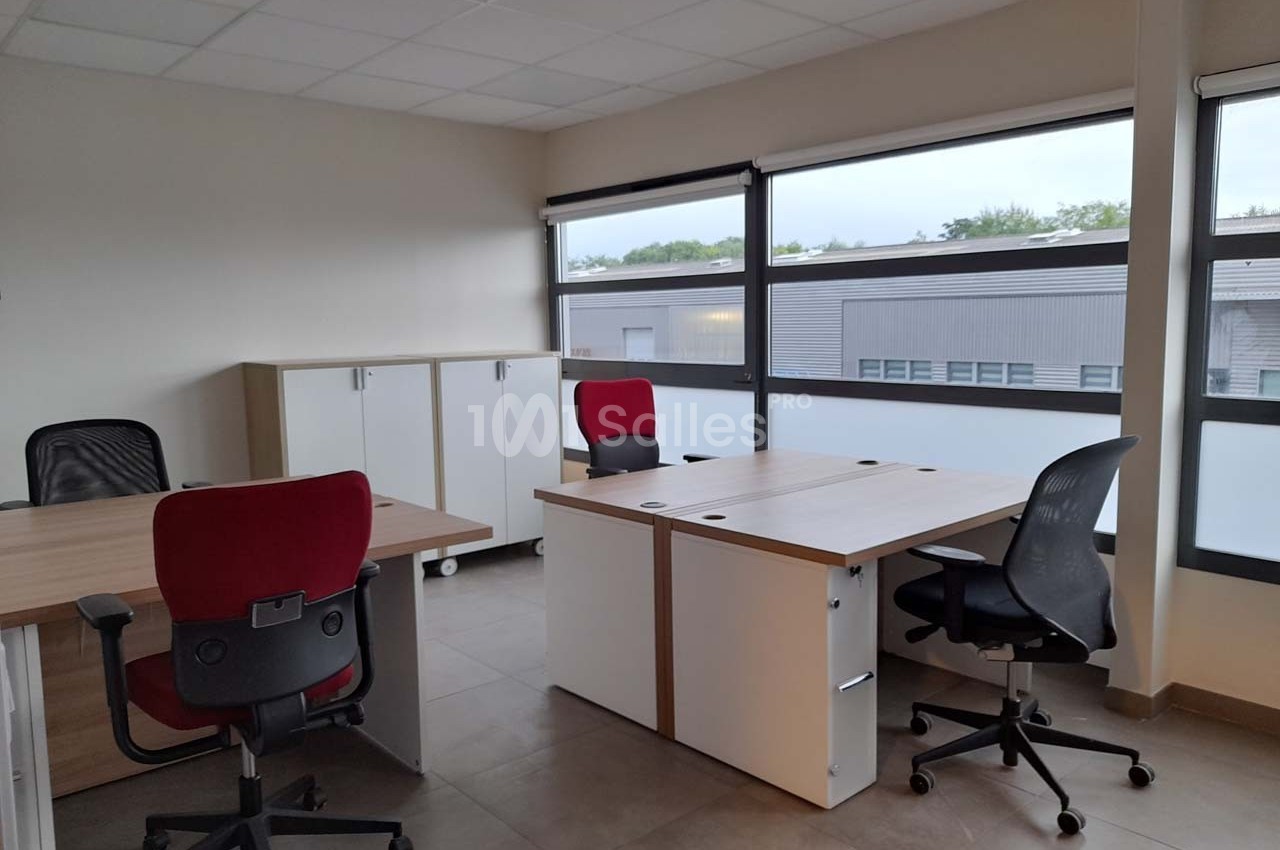 Bureau lumineux avec trois postes de travail équipés de chaises, rangements et grandes fenêtres donnant sur l'extérieur.