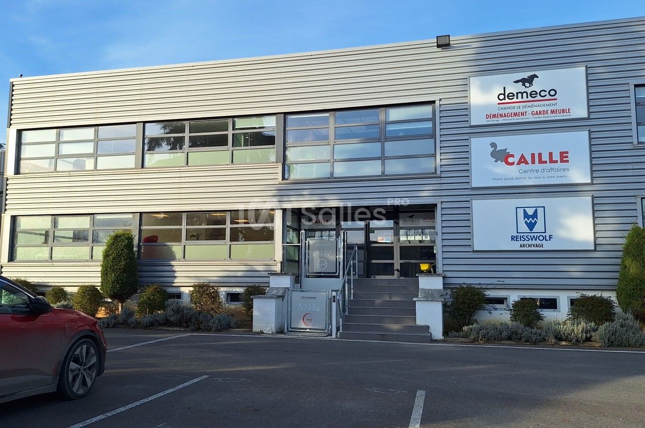 Façade d'un bâtiment commercial avec enseignes de plusieurs entreprises et un parking à l'avant.