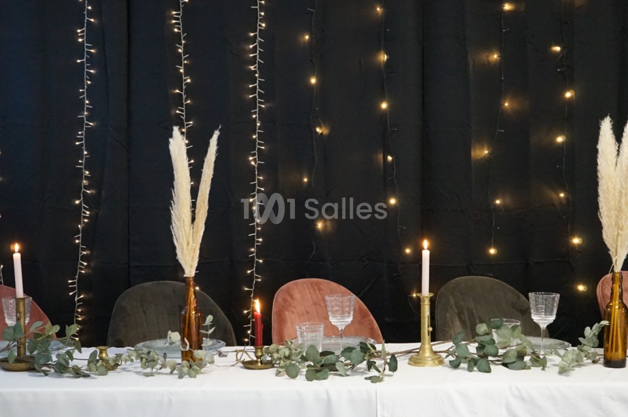 Table décorée avec des chaises colorées, bougies allumées, vases avec herbes de la pampa et guirlandes lumineuses en arrière…