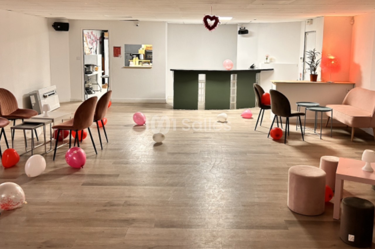 Salle décorée avec des ballons colorés, des chaises et un bar en arrière-plan, éclairée par une lumière douce.