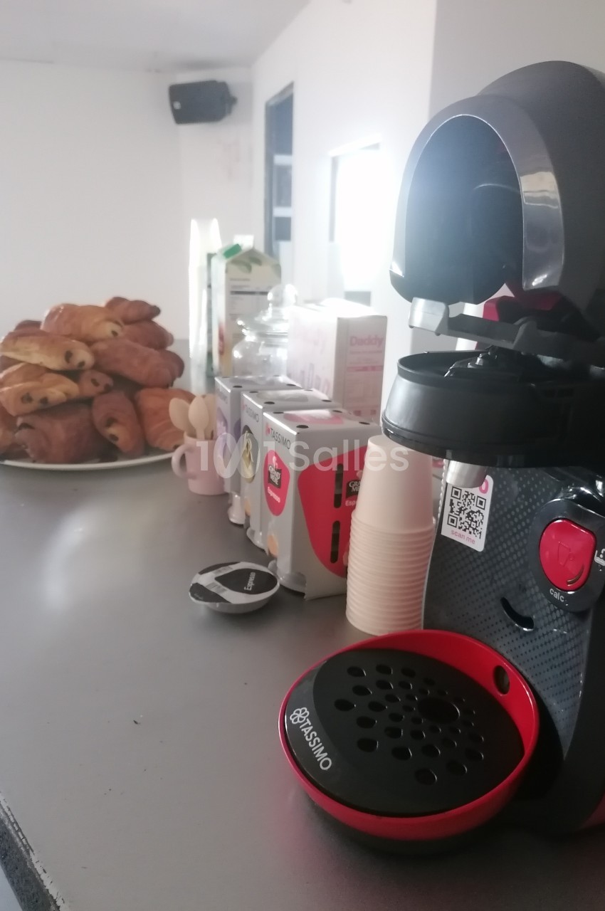 Machine à café rouge et noire sur un comptoir, avec des viennoiseries et des boîtes de capsules en arrière-plan.