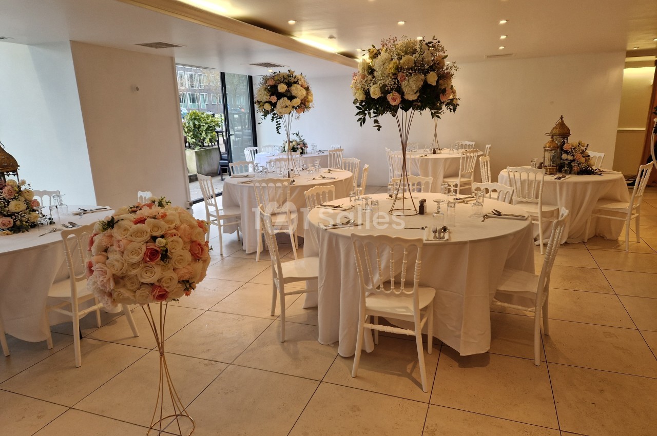 Salle de réception décorée avec des tables rondes, nappes blanches et arrangements floraux élégants.