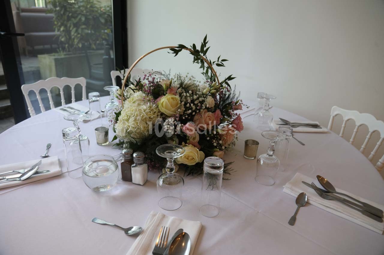 Centre de table floral avec des roses, des hortensias et des feuillages, disposé sur une table dressée avec vaisselle.