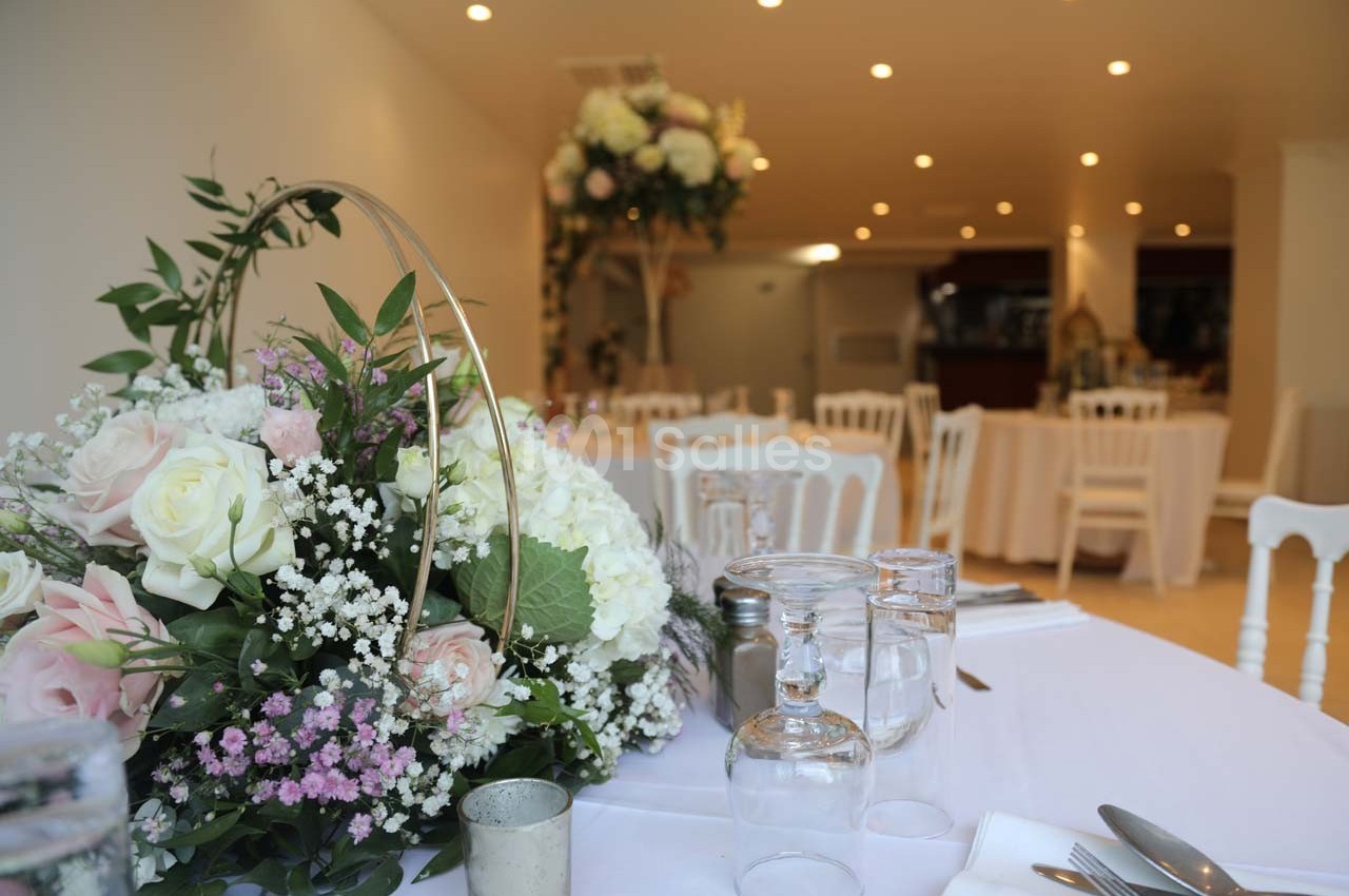 Centre de table floral avec roses et gypsophiles dans une salle de réception lumineuse, décorée pour un événement.