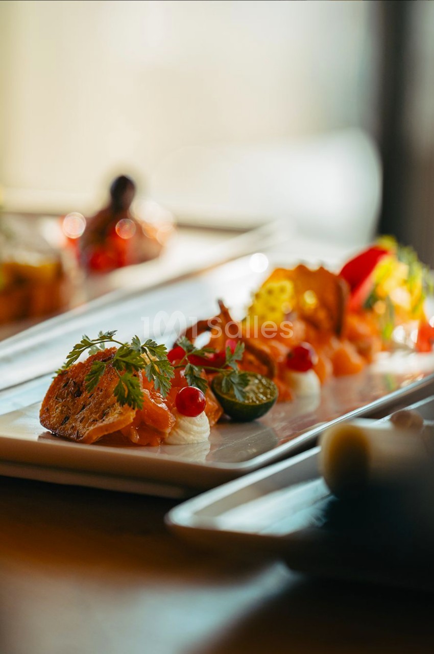 Assiette gastronomique avec des portions de saumon, crème, herbes fraîches et légumes, présentée sur une table lumineuse.