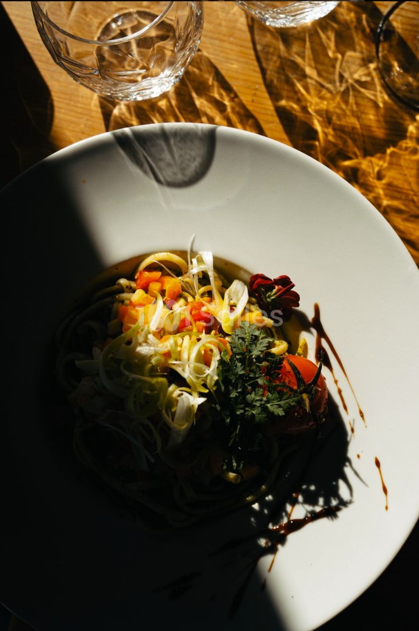 Assiette de pâtes garnie de légumes colorés et herbes fraîches, éclairée par une lumière naturelle partielle.