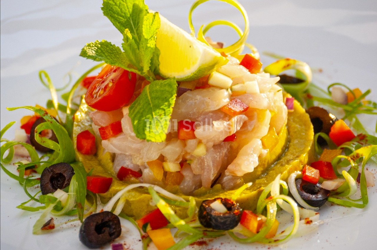 Tartare de poisson blanc avec légumes colorés, olives, citron et menthe, présenté sur une assiette blanche.