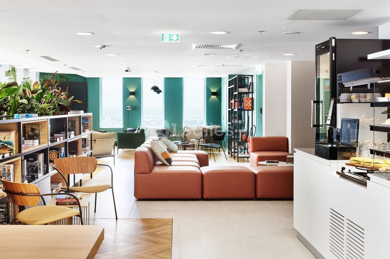 Espace de coworking lumineux avec canapé, étagères, plantes, et coin café équipé dans un décor moderne.