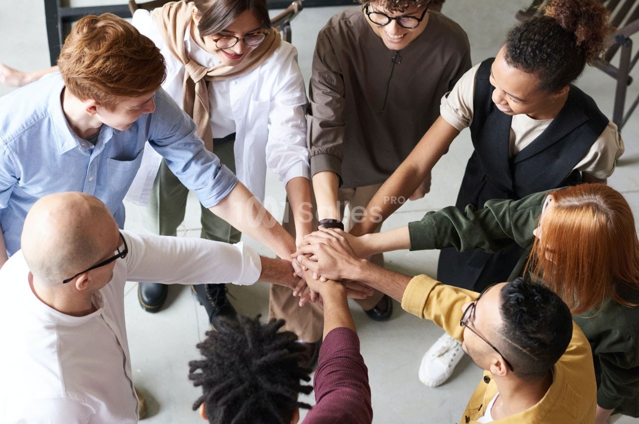Groupe de personnes debout en cercle, joignant leurs mains au centre dans un geste de collaboration.