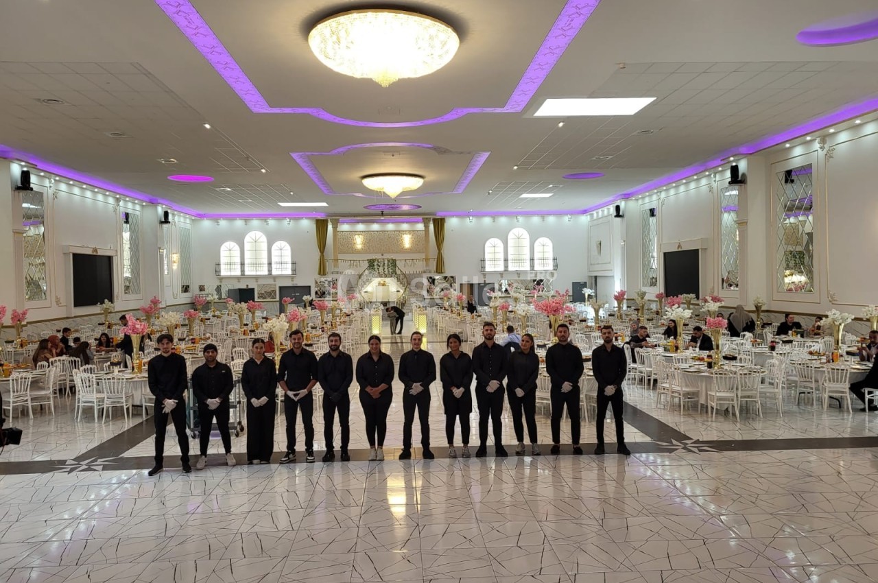 Un groupe de serveurs alignés dans une grande salle de réception décorée avec des tables et des lumières violettes.
